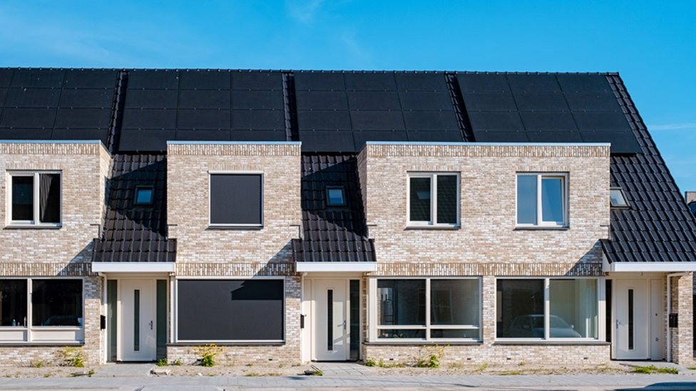 Newly build houses with solar panels attached on the roof against a sunny sky Close up of a new building with black solar panels. Zonnepanelen, Zonne energie, Translation: Solar panel, , Sun Energy.